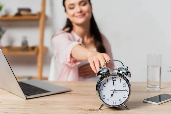 Selective focus of brunette freelancer reaching retro alarm clock — Stock Photo