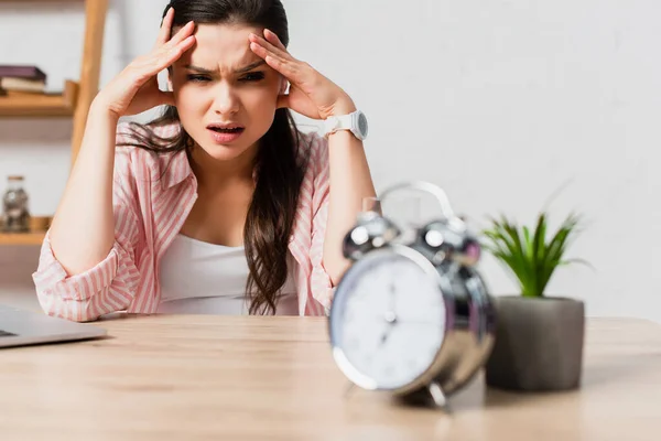 Selective focus of stressed woman touching head near alarm clock and plant — Stock Photo