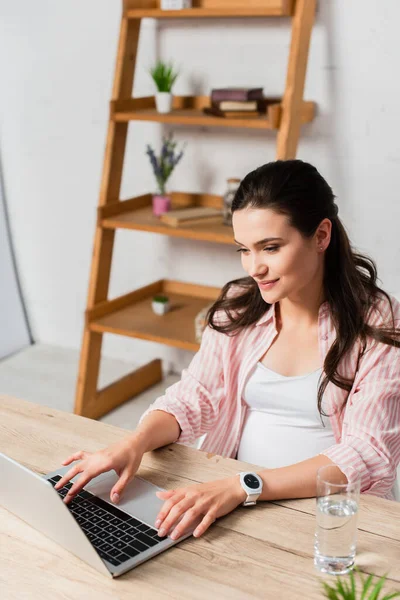 Freelancer grávida usando laptop perto de vidro de água — Fotografia de Stock