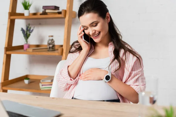 Селективное внимание беременной женщины, говорящей на смартфоне и смотрящей на живот — стоковое фото