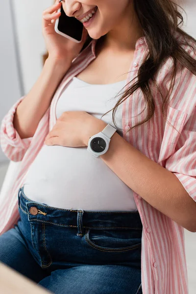 Teilbild einer Schwangeren, die auf dem Smartphone spricht und Bauch berührt — Stockfoto