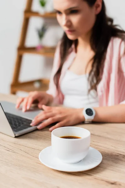 Enfoque selectivo de la taza con café cerca freelancer utilizando el ordenador portátil - foto de stock