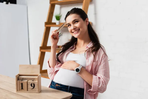 Selektiver Fokus einer Schwangeren, die Bauch in der Nähe von Holzwürfeln mit Datum berührt — Stockfoto