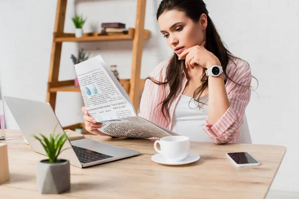 Selective focus of pregnant woman reading newspaper near gadgets and cup on table — Stock Photo
