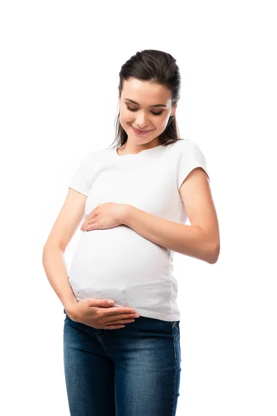 Mujer embarazada en camiseta blanca tocando y mirando el vientre aislado en blanco - foto de stock