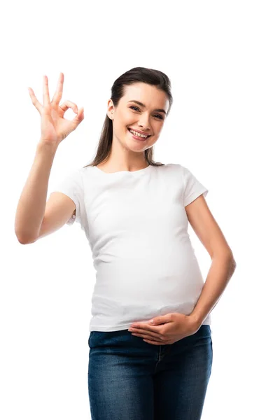 Donna incinta in t-shirt bianca toccare pancia e mostrando segno ok isolato su bianco — Foto stock