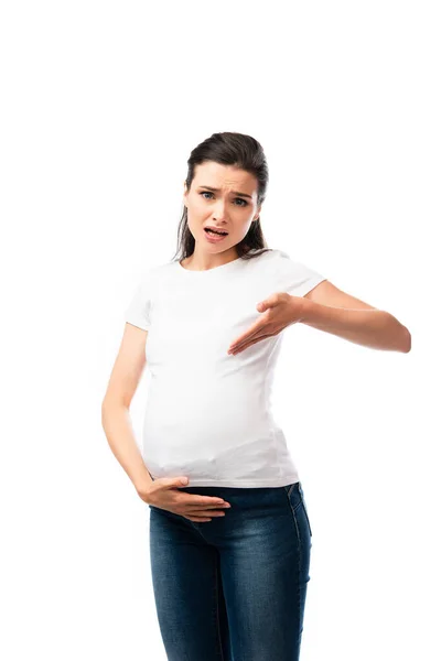 Jeune femme enceinte en t-shirt blanc pointant avec la main sur le ventre isolé sur blanc — Photo de stock