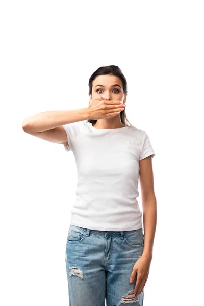 Шокированная женщина в белой футболке и джинсах, покрывающих рот изолированы на белом — стоковое фото