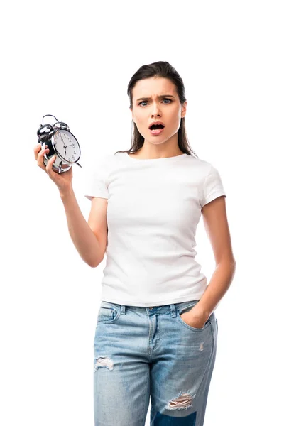 Femme choquée en t-shirt blanc et jeans debout avec la main dans la poche et tenant rétro réveil isolé sur blanc — Photo de stock