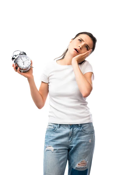 Mujer morena cansada en camiseta blanca y jeans con reloj despertador retro aislado en blanco - foto de stock