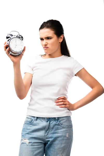 Unzufriedene Frau im weißen T-Shirt mit Retro-Wecker, während sie mit der Hand an der Hüfte isoliert auf weiß steht — Stockfoto