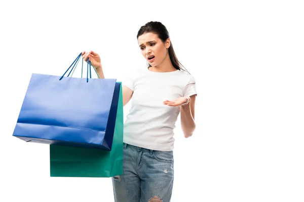 Jovem mulher descontente olhando para sacos de compras isolados em branco — Fotografia de Stock