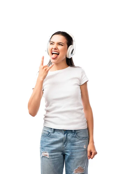 Frau mit drahtlosem Kopfhörer, der die Zunge herausstreckt, während sie Felsschild isoliert auf weiß zeigt — Stockfoto