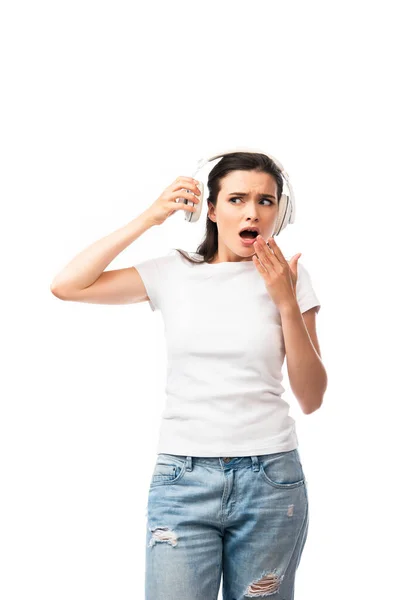 Chocado jovem mulher em branco t-shirt tocando fones de ouvido sem fio isolado no branco — Fotografia de Stock