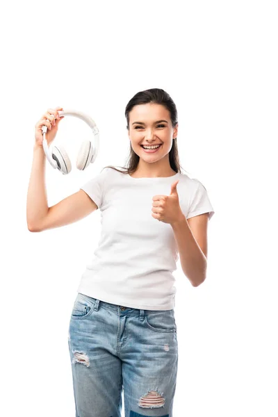 Jovem mulher em t-shirt branca segurando fones de ouvido sem fio e mostrando polegar para cima isolado no branco — Fotografia de Stock
