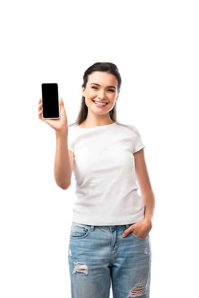 Женщина в белой футболке стоит с рукой в кармане и держит смартфон с пустым экраном изолированы на белом — стоковое фото