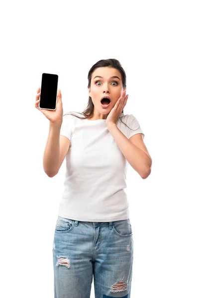 Mujer conmocionada en camiseta blanca sosteniendo teléfono inteligente con pantalla en blanco aislado en blanco - foto de stock