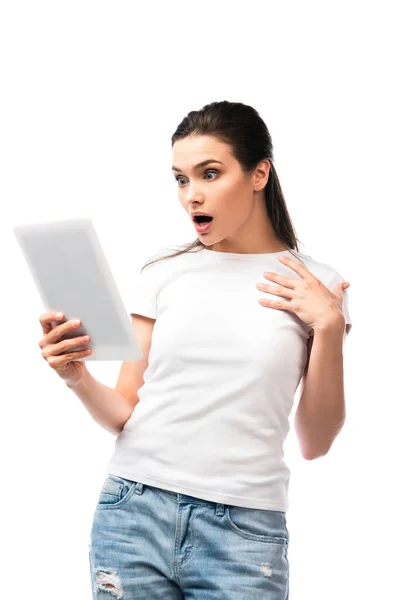 Mujer morena impactada en camiseta blanca usando tableta digital aislada en blanco - foto de stock