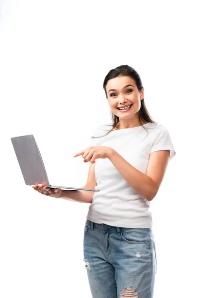 Брюнетка жінка в білій футболці вказує пальцем на ноутбук ізольовано на білому — стокове фото