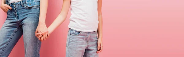 Partial view of woman and kid in jeans holding hands on pink, panoramic shot — Stock Photo