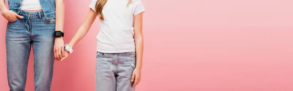 Vue recadrée de la mère et de l'enfant en jeans et smartwatches tenant la main sur rose, en-tête du site — Photo de stock