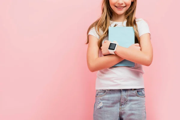 Обрізаний вид дівчини в смарт-годиннику тримає книгу ізольовано на рожевому — стокове фото