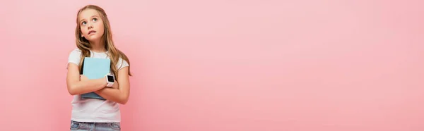 Panamic concept of pensive girl in smartwatch looking away while holding book isolated on pink — стоковое фото
