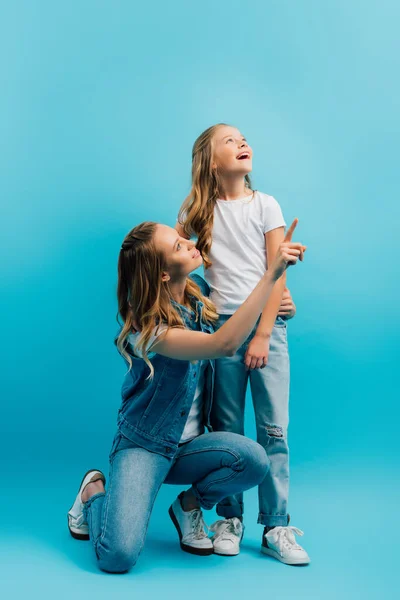 Menina animado olhando para longe perto da mãe apontando com o dedo no azul — Fotografia de Stock