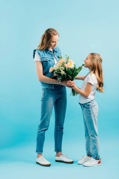 Vista completa del niño en camiseta blanca y jeans presentando flores a la madre en ropa de mezclilla en azul - foto de stock