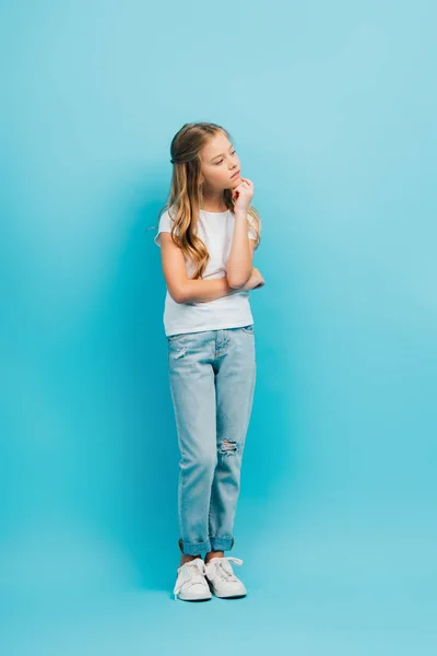 Ganzkörperansicht des nachdenklichen Mädchens in weißem T-Shirt und Jeans, das auf blau wegschaut — Stockfoto