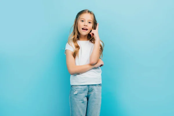 Excited girl with open mouth showing idea gesture while looking at camera isolated on blue — Stock Photo