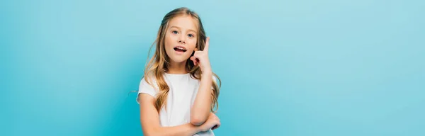 Horizontal image of excited girl in white t-shirt showing idea sign while looking at camera isolated on blue — Stock Photo