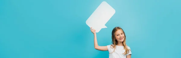 Horizontales Konzept des Kindes, das eine Sprechblase hält und die Kamera isoliert auf blau betrachtet — Stockfoto