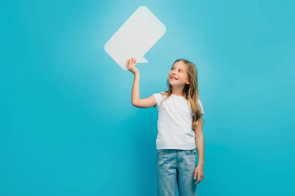 Child in white t-shirt and jeans holding speech bubble isolated on blue — Stock Photo