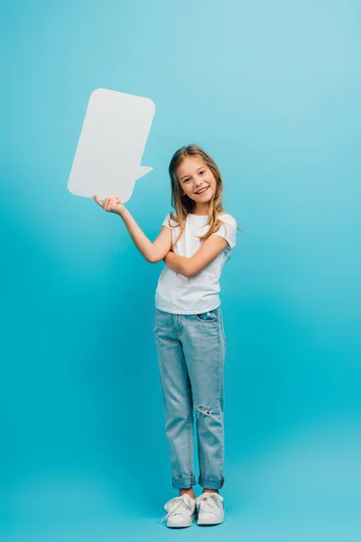 Full length view of girl in jeans and white t-shirt holding speech bubble on blue — Stock Photo