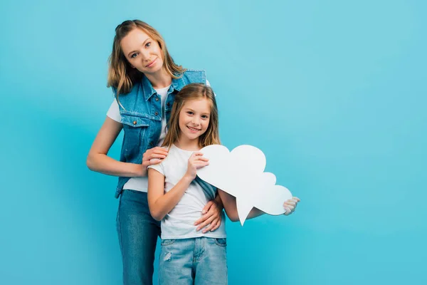 Junge Mutter in Jeansweste umarmt Tochter mit Gedankenblase isoliert auf blau — Stockfoto