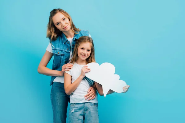 Jeune mère en gilet en denim embrassant fille tenant bulle pensée isolé sur bleu — Photo de stock