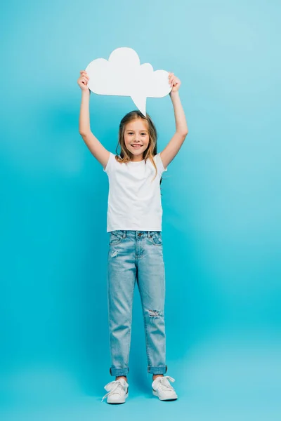 Ganzkörperansicht des Mädchens in Jeans und weißem T-Shirt mit Gedankenblase über dem Kopf auf blau — Stockfoto