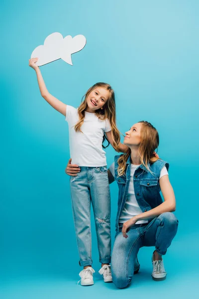 Fille en t-shirt blanc et jeans tenant bulle de pensée près de la mère sur bleu — Photo de stock