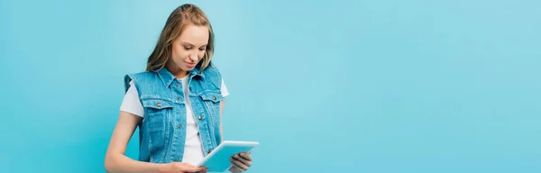 Horizontales Bild einer konzentrierten Frau in Jeansweste mit digitalem Tablet isoliert auf blau — Stockfoto