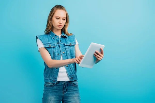 Konzentrierte Frau in Jeansweste mit digitalem Tablet isoliert auf blau — Stockfoto
