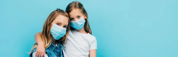 Панорамная концепция ребенка в белой футболке и матери в медицинских масках, смотрящей на камеру, изолированную на голубом — стоковое фото