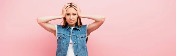 Horizontal image of upset woman touching head while looking at camera isolated on pink — Stock Photo