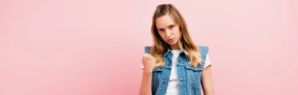 Image horizontale de la femme en colère en gilet en denim montrant poing serré à la caméra isolé sur rose — Photo de stock