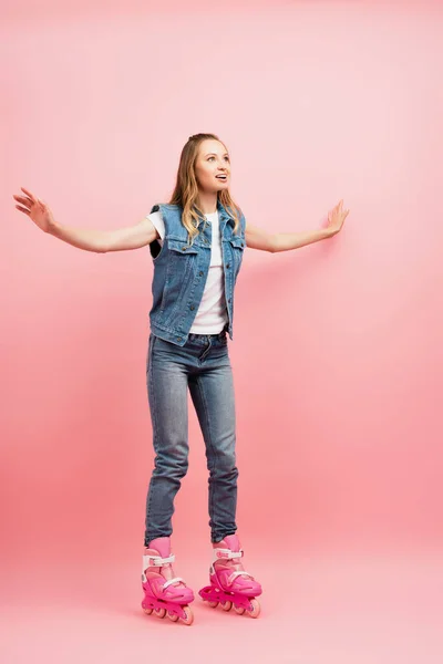 Full length view of excited woman in denim clothes and rollers skates with outstretched hands on pink — Stock Photo