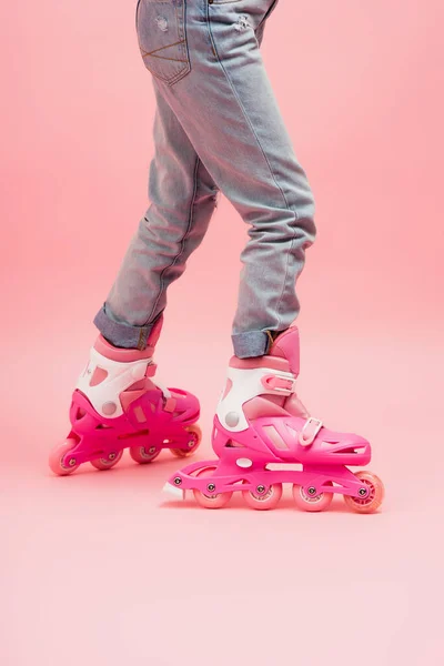 Vue recadrée de l'enfant en jeans et patins à roulettes sur rose — Photo de stock