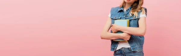 Cropped view of woman in denim vest holding books isolated on pink, horizontal image — Stock Photo