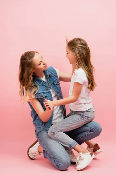 Girl in white t-shirt and jeans sitting on lap of mother on pink — Stock Photo