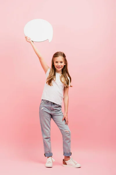 Вид в полный рост девушки в белой футболке и джинсах, держащей мыльный пузырь над головой на розовом — стоковое фото