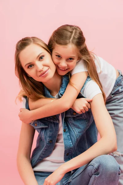 Mädchen umarmt Mutter von hinten, während sie isoliert auf rosa Kamera schaut — Stockfoto